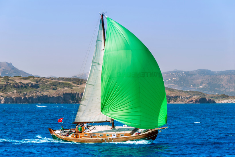 Traditionelles Holzsegelboot mit grünem Segel auf dem türkisblauen Meer vor der Küste der türkischen Ägäis an einem klaren Sommertag