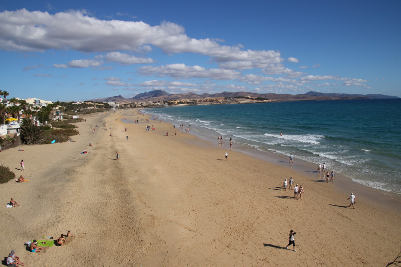 Weitläufiger Sandstrand Playa Barca bei Costa Calma mit Strandbesuchern, Brandung und Bergen im Hintergrund