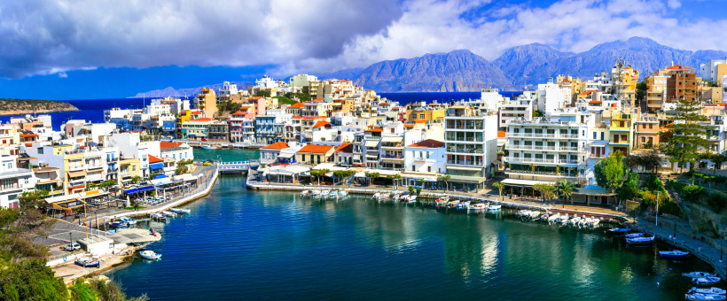 Hafenpromenade von Agios Nikolaos mit Booten, Häusern und Bergen im Hintergrund