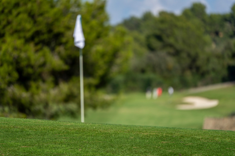 Nahaufnahme eines gepflegten Greens mit Flagge und Bunker auf dem Golfplatz Son Servera bei Cala Bona, umgeben von Pinien und mediterraner Natur.