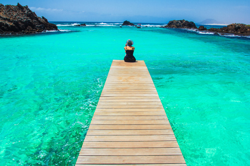 Steg auf Isla de Lobos – Türkisblaues Wasser Person sitzt auf einem Holzsteg über türkisblauem Wasser auf der Isla de Lobos bei Fuerteventura
