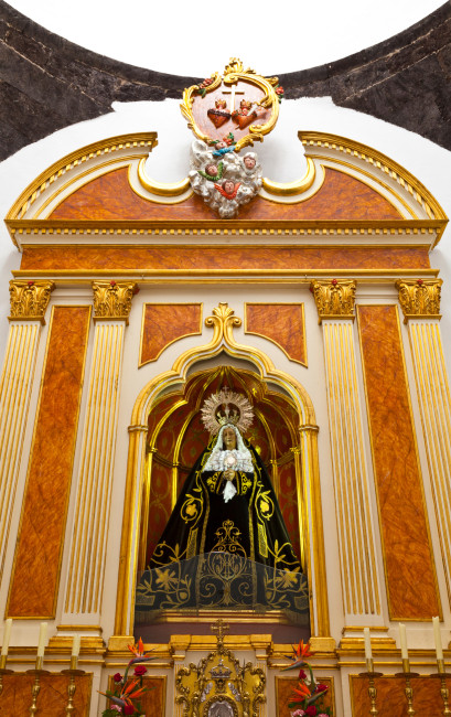 Lanzarote Vergoldeter Altar mit einer Statue der Jungfrau Maria in schwarzem, reich besticktem Gewand. Über der Nische befindet sich ein Symbol mit zwei Herzen, einem Kreuz und Engelsköpfen.