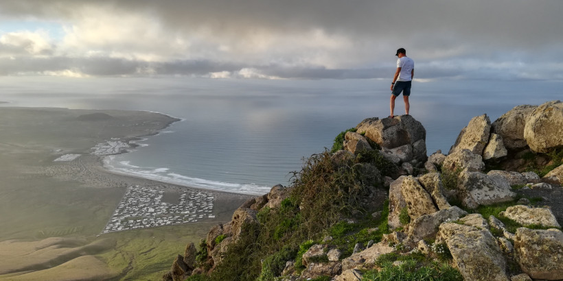 Herbst auf Fuerteventura – Angenehme Temperaturen und beeindruckende Landschaft Wanderer auf einem Felsen über der Küste Fuerteventuras mit weitem Blick auf Meer und Wolken – ideale Zeit für aktive Ausflüge im Herbst.