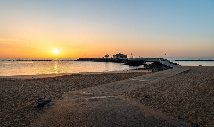 Sonnenaufgang am Strand von Caleta de Fuste mit Holzsteg zur Mole und Pavillon am Meer