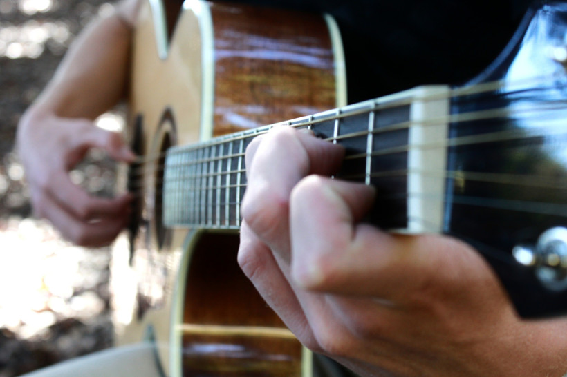 Südafrika Nahaufnahme einer Hand, die auf einer akustischen Gitarre spielt. Die Finger drücken die Saiten auf das Griffbrett, während die andere Hand die Saiten anschlägt.