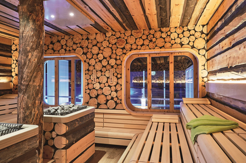 Innenraum der finnischen Sauna an Bord der AIDAnova mit Holzliegen, Saunaofen und Wand aus Holzscheiben