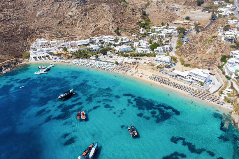 Mykonos - Psarou Beach Strand von Mykonos mit Sonnenschirmen, Liegen und türkisblauem Wasser, umgeben von Hügeln und weißen Häusern