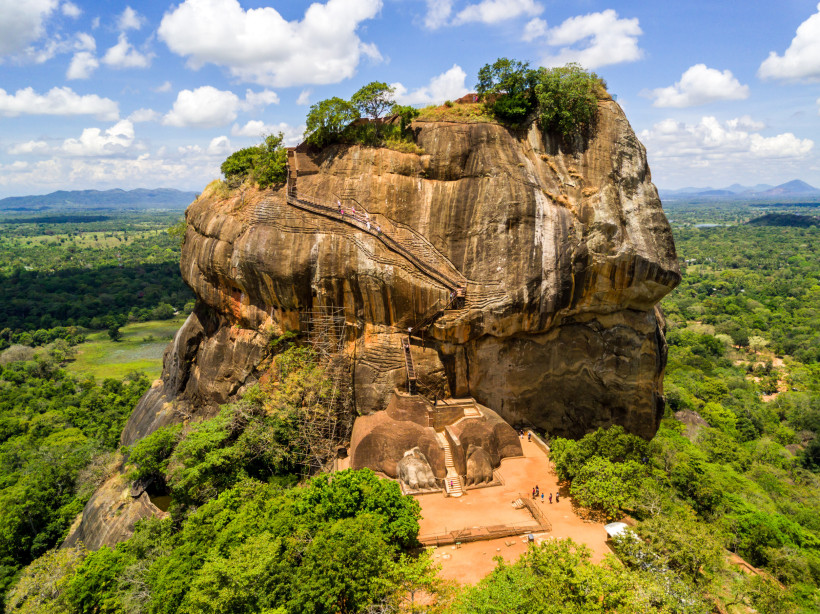 Löwenfelsen, Dambulla, Sri Lanka Majestätische Felsenfestung mit steilen Treppen inmitten tropischer Landschaft, umgeben von grünem Wald und blauem Himmel