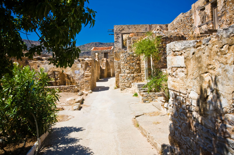 Ruinen und schmale Straße auf der Insel Spinalonga Gasse zwischen verfallenen Steinhäusern auf Spinalonga bei blauem Himmel