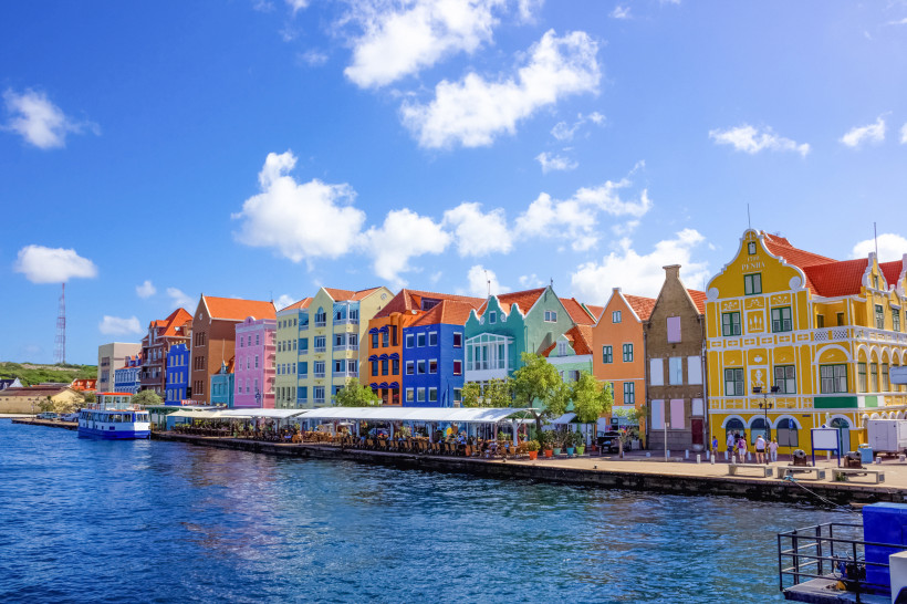 Uferpromenade in Willemstad auf Curaçao mit bunten Kolonialhäusern am Wasser unter blauem Himmel