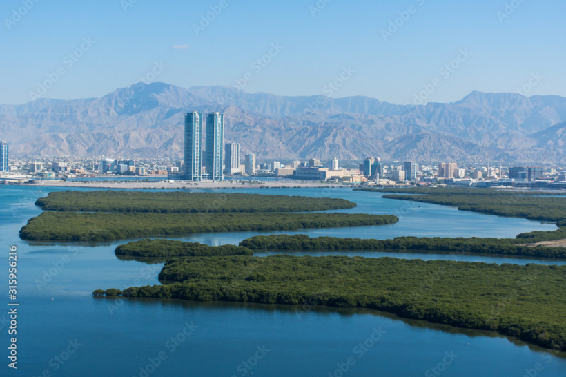Ras al Khaimah, budgetfreundlicher Urlaub Luftaufnahme einer Stadt mit Hochhäusern, Mangroveninseln und Bergen im Hintergrund