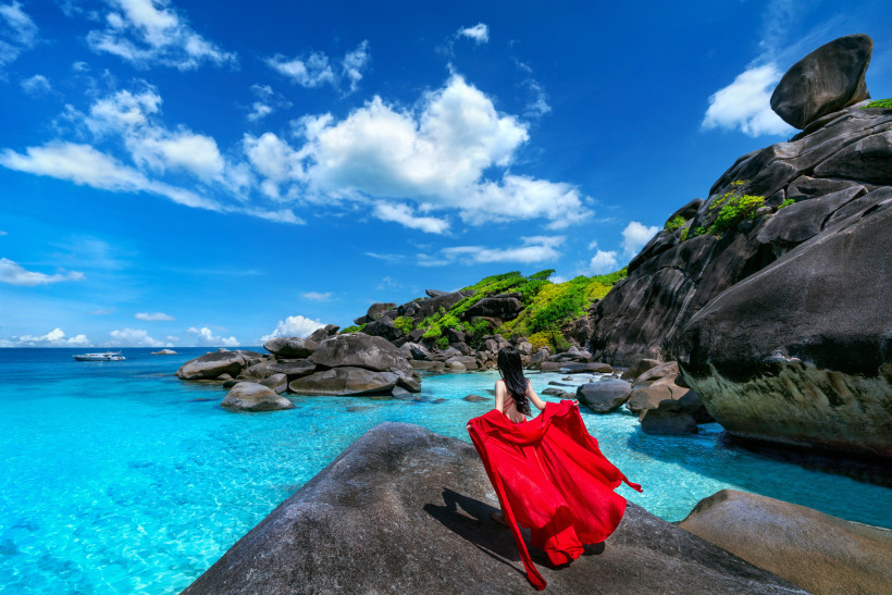 Similan Islands bei Khao Lak – kristallklares Wasser und Felsenlandschaft Frau in rotem Kleid steht auf Felsen mit Blick auf das türkisfarbene Wasser der Similan Islands bei Khao Lak, Thailand.