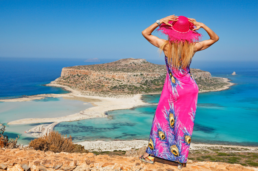 Lagune von Balos mit Sandbank und Felseninsel, aufgenommen vom Aussichtspunkt Blick vom Aussichtspunkt auf die Lagune von Balos mit türkisfarbenem Wasser und Sandbank, im Vordergrund Person in pinkem Kleid