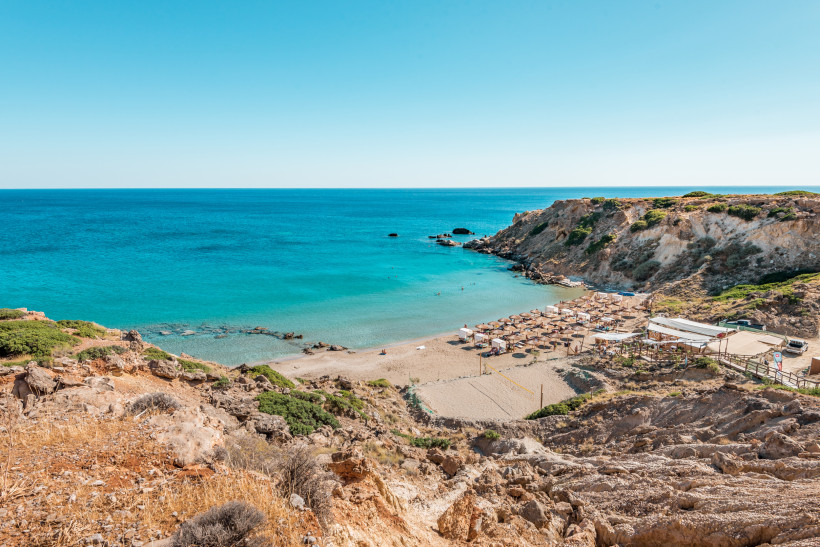 Strandbucht mit Sonnenschirmen und türkisblauem Wasser auf Kreta, umgeben von Felsen