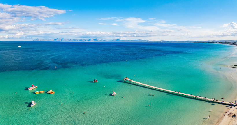 Luftaufnahme der Platja d’Alcúdia mit türkisfarbenem Wasser, Badesteg und flachem Sandstrand
