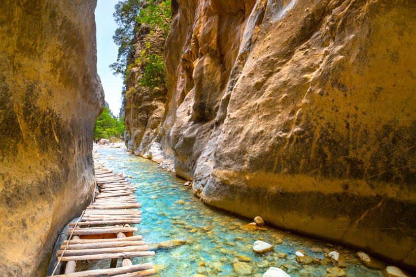 Holzsteg entlang eines klaren Flusses zwischen hohen Felswänden in der Samaria-Schlucht