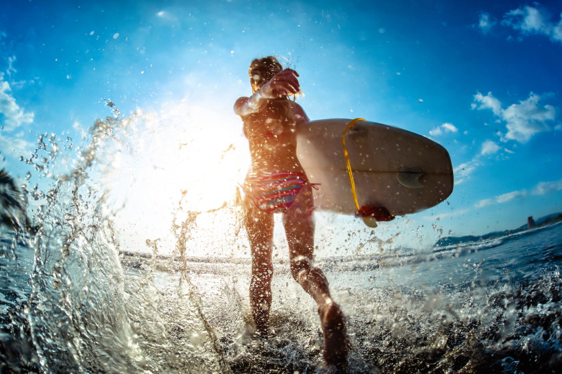 Costa Rica Surferin mit Surfbrett läuft durch spritzendes Wasser bei Sonnenlicht, mit blauem Himmel im Hintergrund