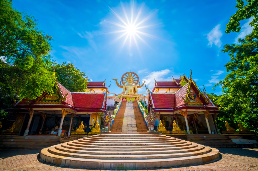 Treppenaufgang zum Wat Phra Yai Tempel auf Koh Samui, Thailand, mit goldener Buddha-Statue und traditioneller Architektur unter strahlender Sonne.