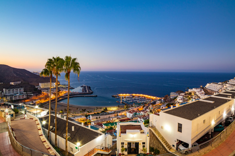 Abendlicher Blick auf den Hafen und die Bucht von Puerto Rico auf Gran Canaria mit Palmen und Küstenbebauung