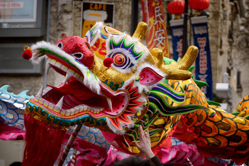 eindrucksvolle Darstellung eines chinesischen Drachentanzes während einer Parade. Der Drache ist farbenprächtig gestaltet mit einem goldglänzenden Kopf, roten Augen, aufwendigen Mustern und goldenen Hörnern. Sein offenes Maul mit scharfen Zähnen und einer