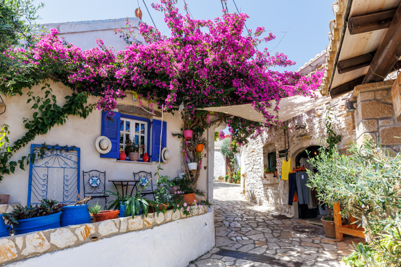 Idyllisches weißes Haus mit blauen Fensterläden und blühender Bougainvillea in einer engen Gasse auf einer griechischen Insel