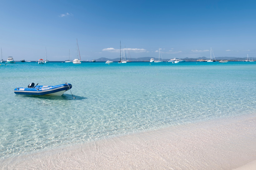 Klares, türkisfarbenes Meer und heller Sandstrand auf Formentera mit Booten vor der Küste