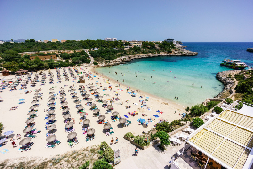 Buchtstrand in Portocolom mit Sonnenschirmen, Badenden und türkisfarbenem Meer