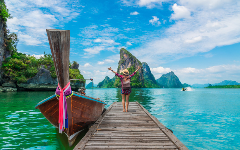 Thailand Reisearten – Longtailboot Frau auf Holzsteg vor einem Longtailboot in türkisblauem Meer, umgeben von tropischen Felsen – ideales Motiv für Thailand Reisearten wie Strandurlaub, Inselhopping und Aktivurlaub.