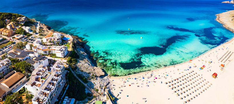 Luftaufnahme der Cala Mesquida auf Mallorca mit hellem Sandstrand, Sonnenliegen und türkisfarbenem Meer