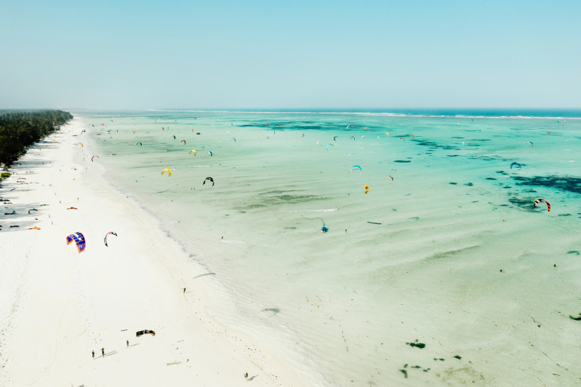 Sansibar - Paje Weißer Sandstrand auf Sansibar mit türkisblauem Meer voller Kitesurfer – beliebter Spot für Wassersport und Aktivitäten im Urlaub in Tansania