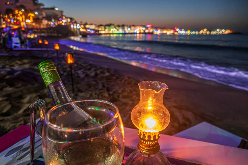 Abendessen bei Kerzenlicht am Strand von Chersonissos Romantische Abendstimmung am Strand von Chersonissos mit Laternenlicht und Weinflasche im Vordergrund