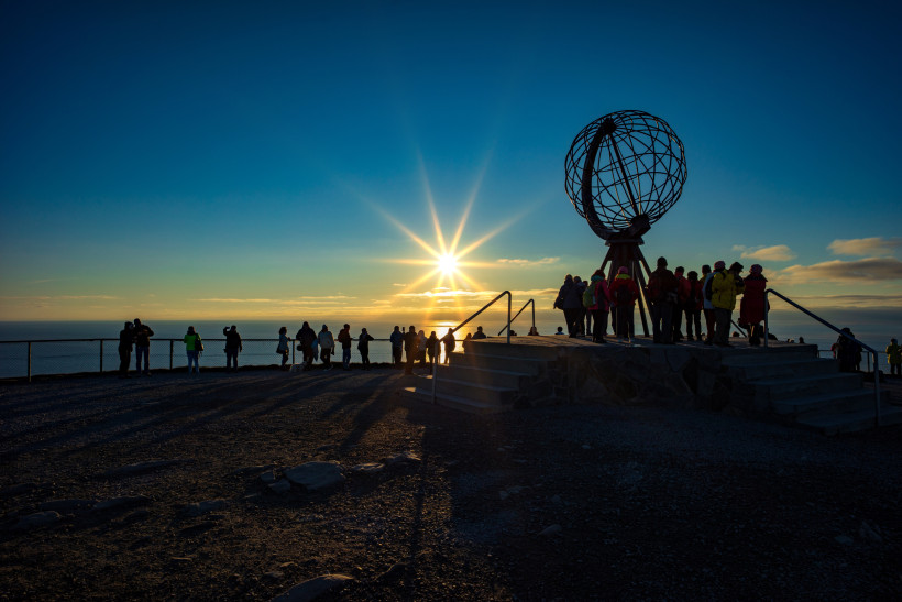 Nordkap-Plateau mit Globus-Skulptur und Besuchergruppe bei Mitternachtssonne über dem Meer