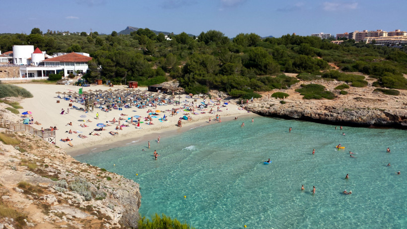 Cala Domingos in Calas de Mallorca mit hellem Sandstrand, Liegenbereich und flach abfallendem, klarem Wasser.