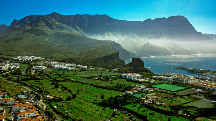Agaete – spektakuläre Landschaft zwischen Bergen und Meer auf Gran Canaria Blick auf Agaete im Nordwesten von Gran Canaria mit grünen Feldern, weißen Häusern und dem imposanten Bergmassiv im Hintergrund. Die Küste und der Atlantik glitzern in der Sonne – ein eindrucksvolles Panorama der Kanaren.