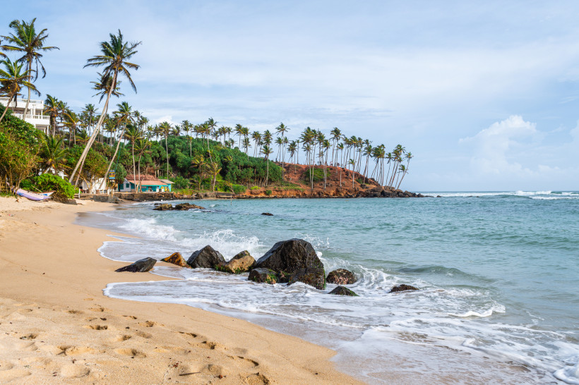 Mirissa, Sri Lanka Tropischer Sandstrand mit Palmen und Felsen in Mirissa, Sri Lanka, mit sanften Wellen des Indischen Ozeans