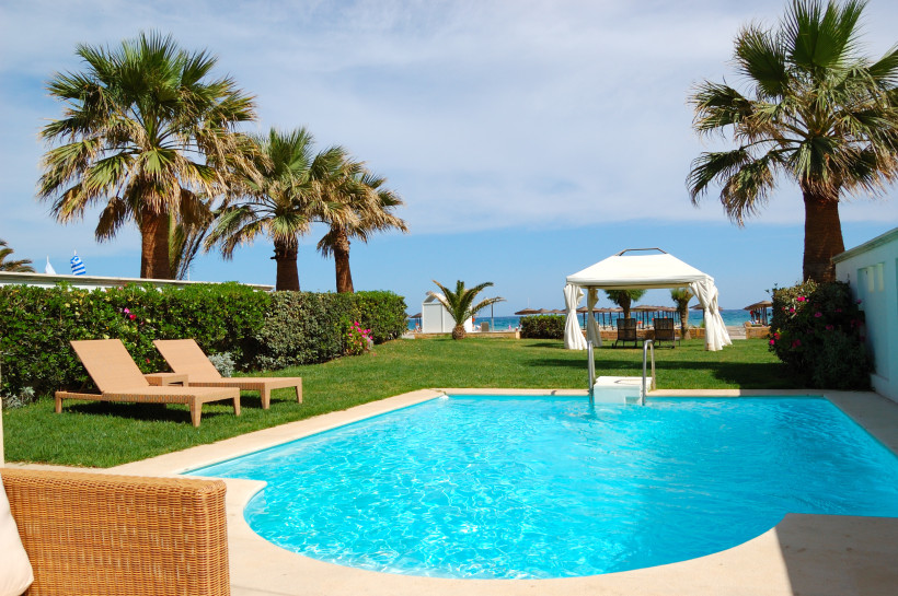 Ägypten - Sharm el Sheikh Ein privater Gartenbereich mit zwei Sonnenliegen, einem kleinen Pool und einem weißen Pavillon mit Blick auf das Meer. Palmen, gepflegter Rasen und bunte Blumen umgeben den Pool. Im Hintergrund sieht man den Strand mit Sonnenschirmen und das türkisfarbene