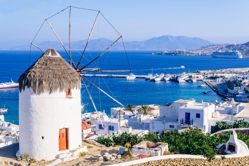 Windmühle mit Strohdach oberhalb des Hafens von Mykonos, mit weißen Häusern und Yachten am blauen Meer