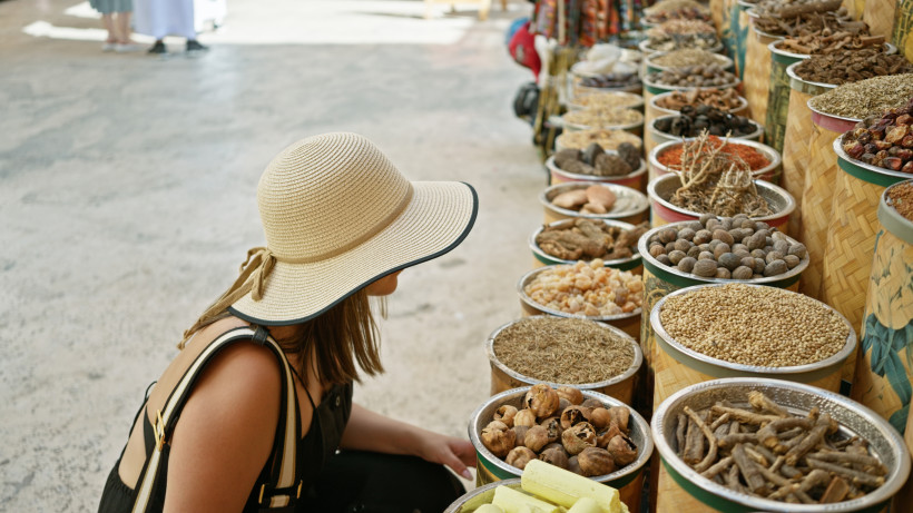 Dubai Eine junge Frau mit Strohhut erkundet einen traditionellen Souk in Dubai zwischen bunten Gewürzen und Stoffen.