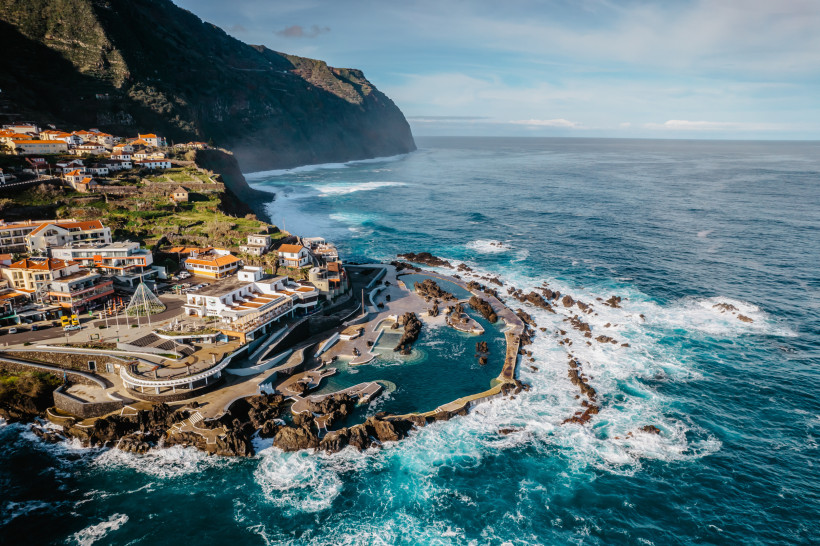 Küstenansicht von Porto Moniz auf Madeira mit vulkanischen Lavapools am Atlantik und umliegenden Häusern