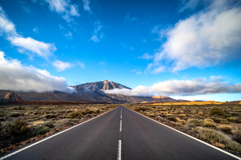 Lange gerade Straße Richtung Vulkan Teide unter blauem Himmel mit Wolken