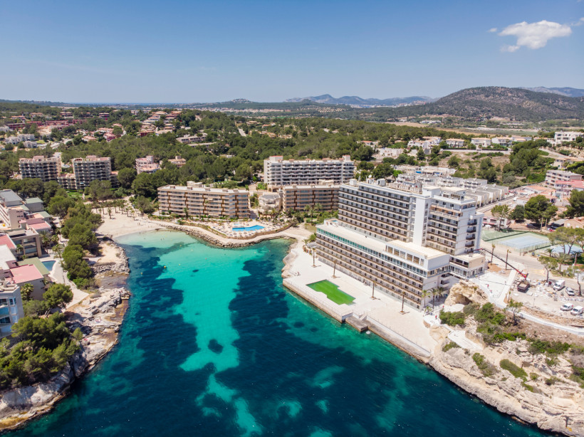Luftaufnahme der Bucht Cala Vinyes mit türkisfarbenem Wasser, Hotels am Ufer und bewaldeter Umgebung