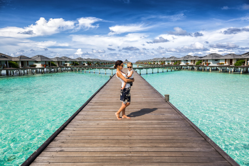Steg über türkisfarbenem Wasser mit Wasserbungalows im Ari-Atoll