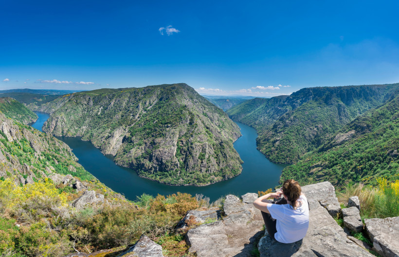 Blick auf eine Flussschleife in der Ribeira Sacra mit steilen, bewaldeten Felswänden und Person auf einem Aussichtspunkt