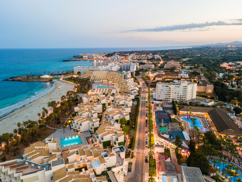 Luftaufnahme von Sa Coma am Abend mit Strand, Hotelanlagen und beleuchteter Küstenstraße