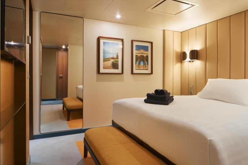 Costa Smeralda Grand Suite – Schlafzimmer mit Doppelbett und Sitzbank Schlafbereich der Grand Suite auf der Costa Smeralda mit Doppelbett, Sitzbank und Wandbildern