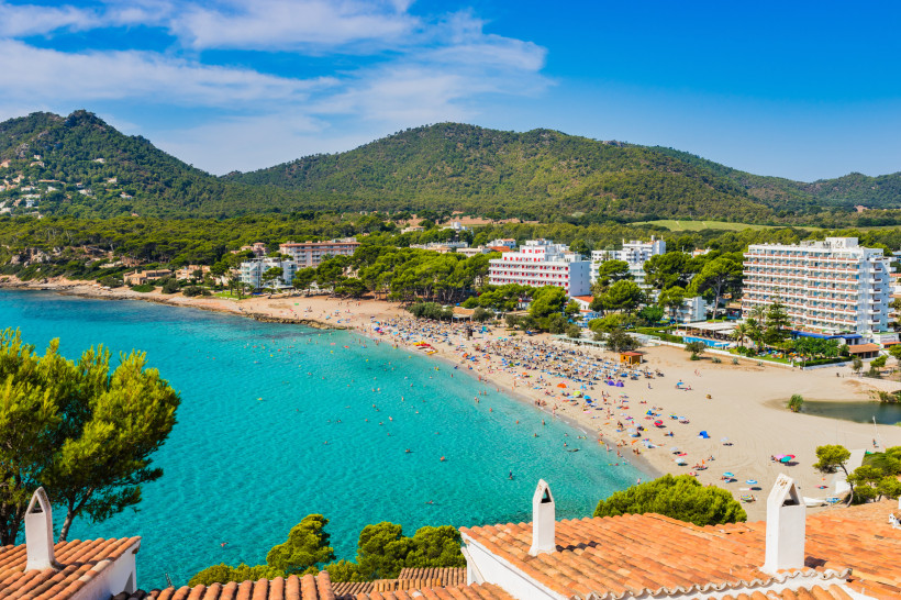 Bucht und Sandstrand in Canyamel mit Badegästen, Hotels und bewaldeten Hügeln im Hintergrund