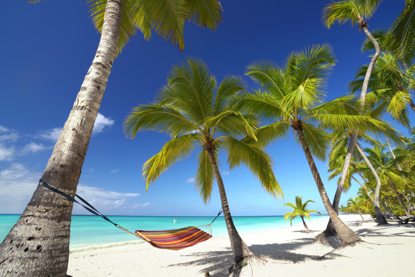 Dom.Rep. Bunte Hängematte zwischen Palmen an einem tropischen Sandstrand mit türkisfarbenem Meer und strahlend blauem Himmel