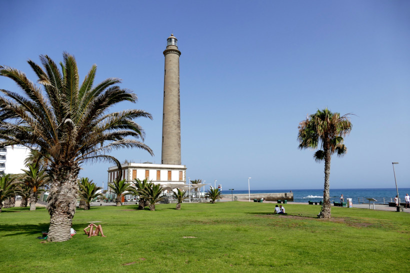 Leuchtturm Faro de Maspalomas mit Palmen und Grünfläche am Meer