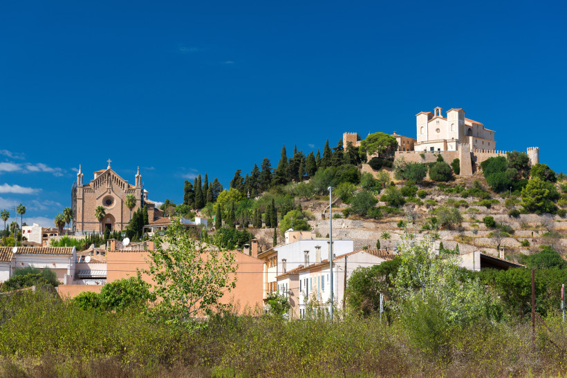 Santuari de Sant Salvador auf einem Hügel über Häusern und Vegetation unter blauem Himmel