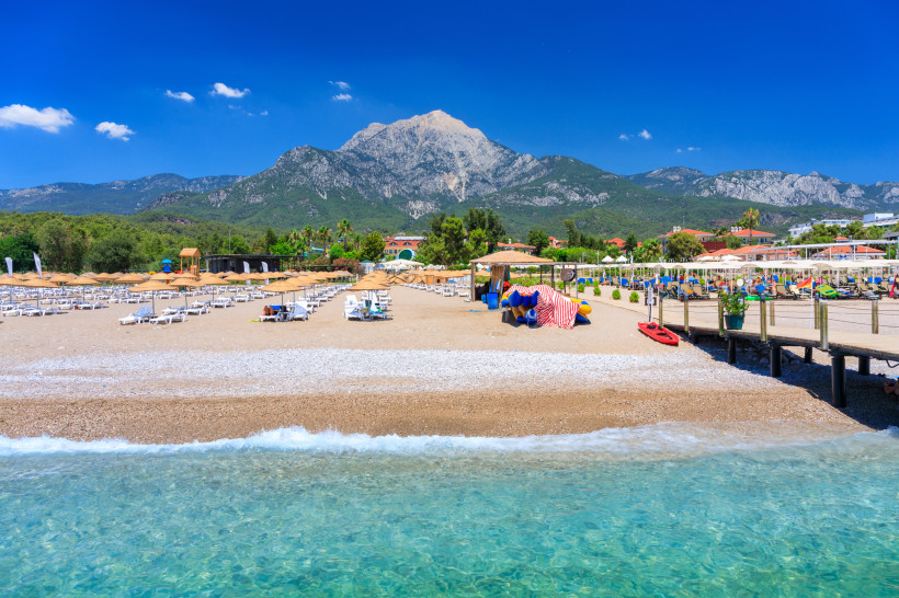 Kiesstrand in Kemer mit Sonnenliegen, klarem Wasser und Bergen im Hintergrund
